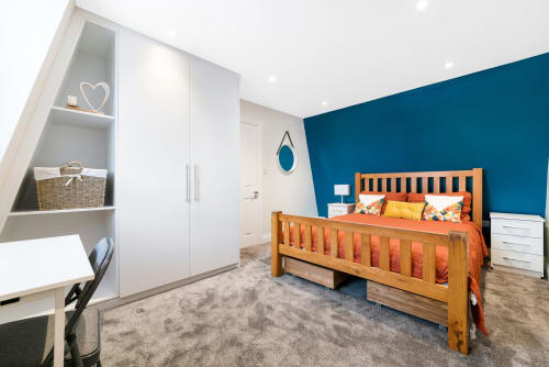 Modern bedroom at Creative Living Rooms London with teal accent wall, wooden bed, white wardrobe and built-in shelving