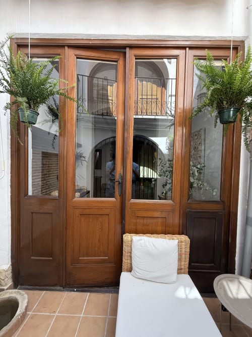 Puertas de cristal de madera con helechos colgantes abriéndose a un patio en Hotelito Oliva Pensión, Oliva, España