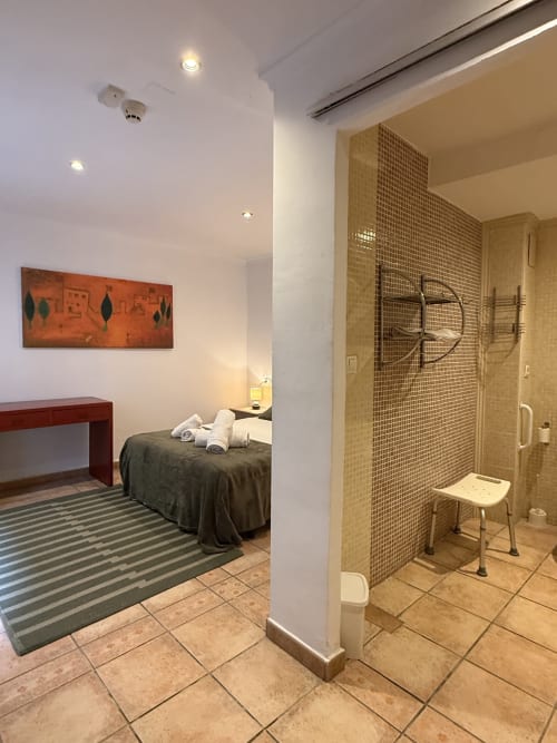 Habitación accesible en Hotelito Oliva con dormitorio, baño con barras de seguridad y silla de ducha, comodidades modernas y vistas de la ciudad
