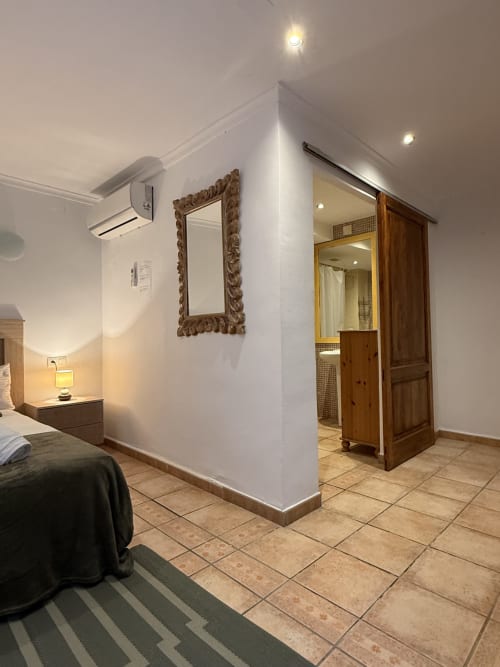 Habitación moderna de Hotelito Oliva con baño privado, paredes blancas, puerta de madera y espejo decorativo