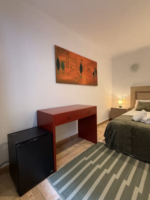 Habitación doble en Hotelito Oliva con escritorio rojo, TV y cama en hotel frente al mar en Oliva, España