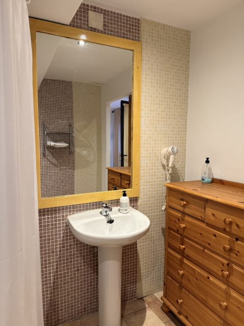 Baño moderno en Hotelito Oliva Pensión con lavamanos pedestal, espejo marco amarillo y paredes con azulejos mosaico en Oliva, España