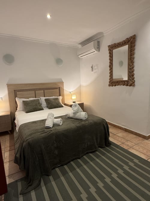 Moderno dormitorio doble en Hotelito Oliva Pensión en Oliva con cama de madera, ropa de cama oscura, espejo ornamentado y alfombra rayada