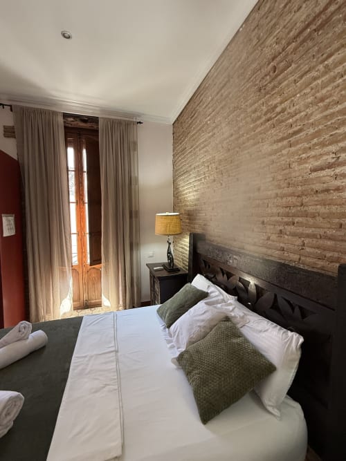 Habitación moderna del Hotelito Oliva con pared de ladrillo visto, cama Queen, puertas de madera y vistas a la ciudad en Oliva, España