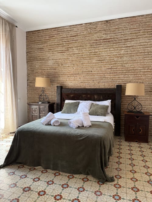 Elegante habitación doble en Hotelito Oliva con pared de ladrillo, cama de madera oscura, lámparas gemelas y piso de azulejos estampados