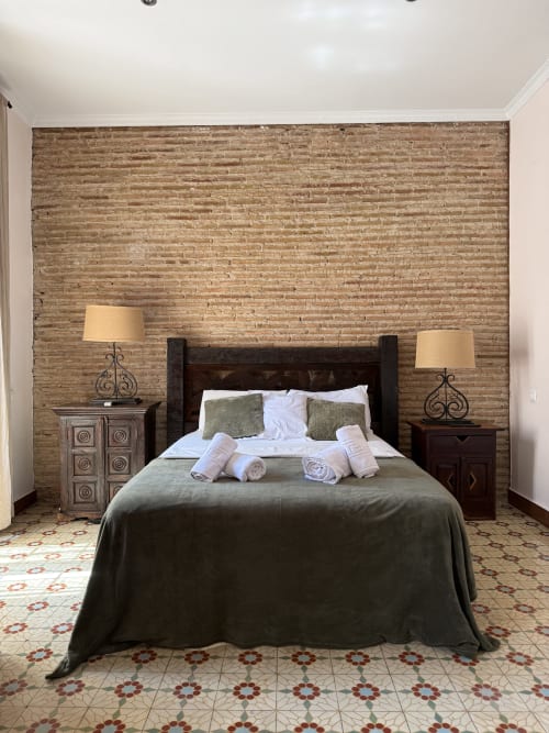 Habitación doble en Hotelito Oliva Pensión con pared de ladrillo visto, cama de madera oscura, lámparas gemelas y baldosas de patrón decorativo