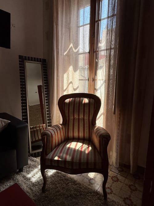 Sillón a rayas en habitación soleada del Hotelito Oliva con vista al balcón y paisaje urbano