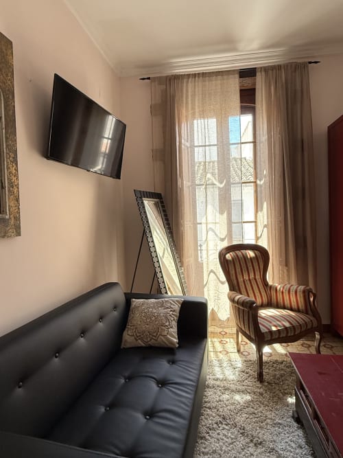 Habitación moderna en Hotelito Oliva con sofá negro, butaca rayada, TV en pared y balcón con vistas a la ciudad de Oliva