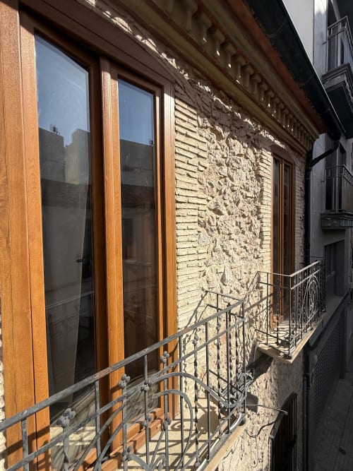 Balcón con barandilla de hierro forjado en Hotelito Oliva Pensión, con puertas de madera y fachada de ladrillo terracota