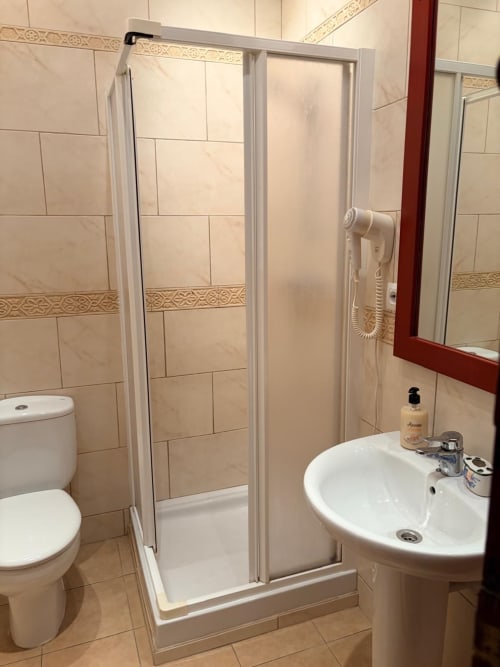 Baño moderno con ducha, lavabo blanco tipo pedestal, inodoro y espejo con marco rojo en Hotelito Oliva Pensión de Oliva