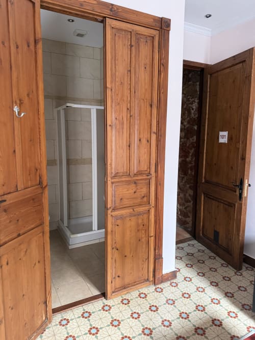 Entrada al baño de la Habitación 101 en Hotelito Oliva Pensión, Oliva, con puertas de madera, piso de azulejos y ducha visible