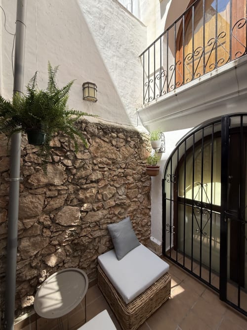 Acogedor patio exterior de Hotelito Oliva Pensión en Oliva, España, con muro de piedra rústica, mobiliario de mimbre y herrería