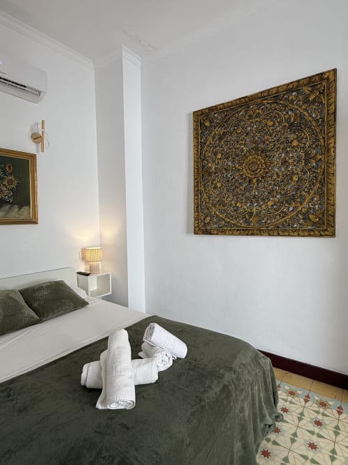 Elegante habitación en Hotelito Oliva Pensión con ropa de cama verde oliva, toallas blancas enrolladas, arte mural ornamental dorado y