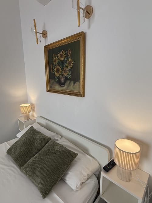 Dormitorio minimalista en Hotelito Oliva con almohadas verdes, cuadro de girasoles, lámparas de pared en latón e iluminación de mesita de noche