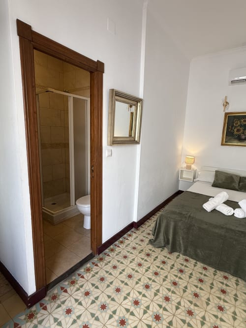 Habitación doble con baño en-suite del Hotelito Oliva, cama con ropa de cama verde, baldosas de piso estampadas y espejo en Oliva, España