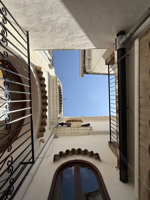 Estrecho patio del Hotelito Oliva Pensión en Oliva, España, con paredes encaladas, barandillas ornamentales y cielo azul despejado