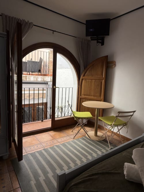Habitación moderna con puertas arqueadas de madera que abren a balcón, mesa redonda con sillas, TV y vistas a la ciudad en Hotelito Oliva