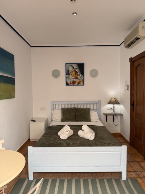 Moderno dormitorio doble en Hotelito Oliva Pensión en Oliva con cama blanca, ropa de cama oscura, toallas enrolladas, lámpara de mesita y