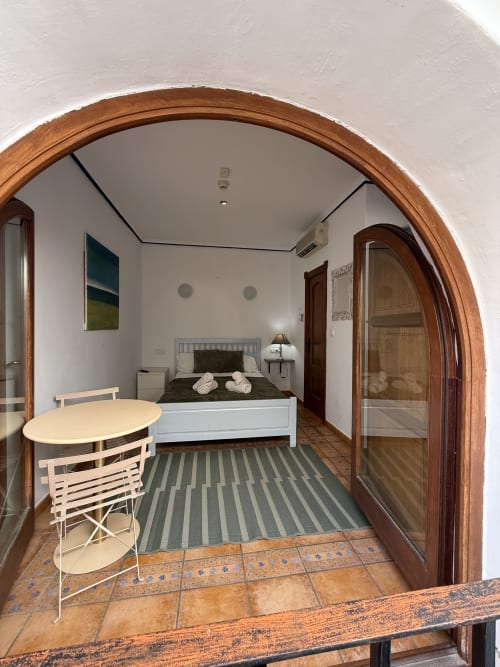 Habitación doble en Hotelito Oliva Pensión en Oliva con cama, escritorio, alfombra rayada y entrada con puerta arqueada de madera
