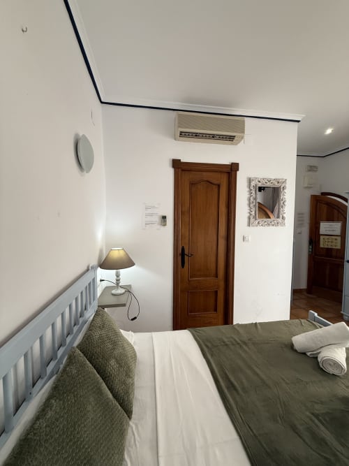 Habitación doble en Hotelito Oliva Pensión en Oliva con cama, aire acondicionado, lámpara de escritorio, puerta de madera y barandillas blancas