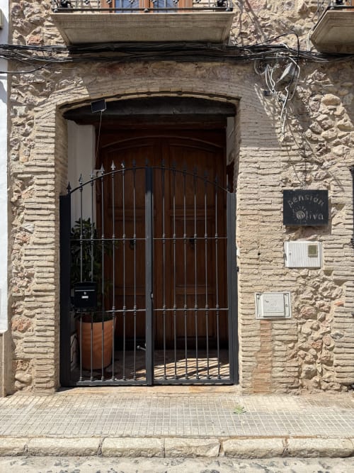 Entrada de Hotelito Oliva Pensión en Oliva, España, con fachada de piedra tradicional, puerta de madera oscura y herrajes de hierro