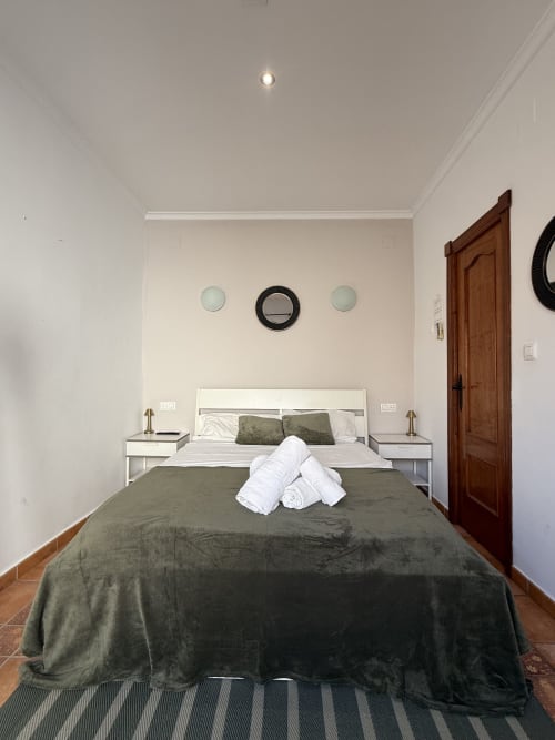 Dormitorio doble moderno en Hotelito Oliva Pensión con colcha verde, mesitas blancas y espejos decorativos en Oliva
