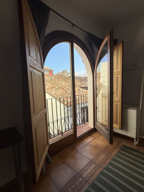Puertas dobles arqueadas abren a un balcón con vistas a los tejados de terracota de Oliva, España en Hotelito Oliva Pensión