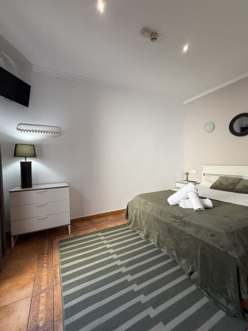 Moderna habitación doble en Hotelito Oliva Pensión en Oliva con cama, cómoda, lámpara, TV de pantalla plana e iluminación contemporánea