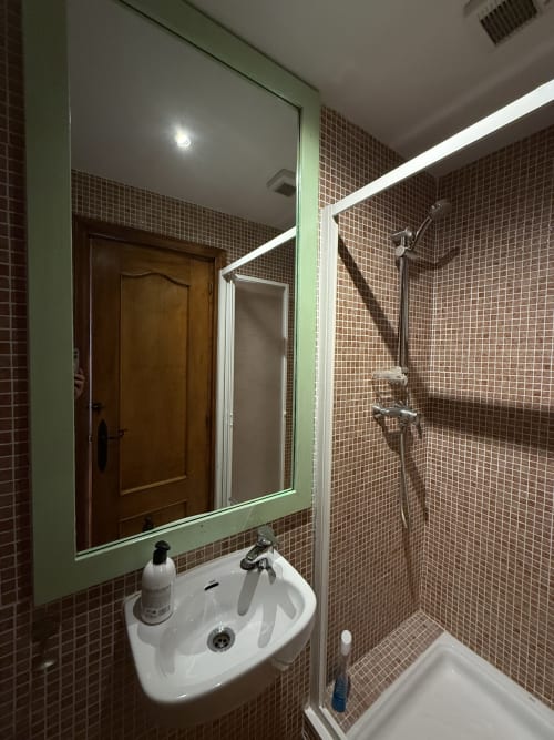 Baño moderno con azulejos de mosaico marrón, espejo con marco verde, lavabo blanco y ducha en Hotelito Oliva Pensión en Oliva