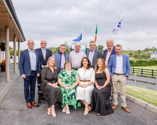 Group of nine people posing outside Sliabh Beagh Hotel with Irish and EU flags in Monaghan