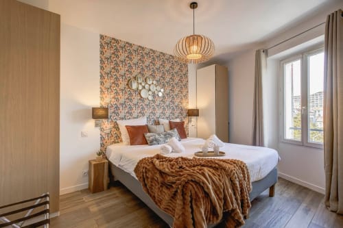 Elegantes Schlafzimmer in Cannes mit gemusterter Akzentwand, Pendelleuchte und Stadtblick von den Balkontüren