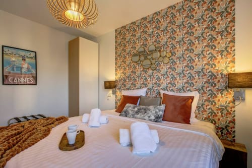 Stilvolles Schlafzimmer im Luxusapartment TOTO LULU Cannes mit Musterthapete, weißen Handtüchern auf dem Bett und warmer Atmosphäre