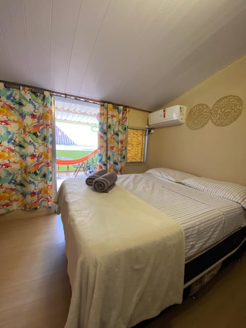 Quarto iluminado na Pousada New Ipanema com camas de casal, cortinas coloridas, ar-condicionado e vista da varanda para o Rio de Janeiro