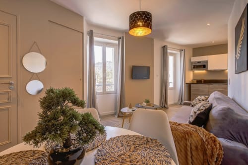 Modernes Studio-Apartment in Cannes mit warmen beigefarbenen Wänden, gemütlichem Wohnbereich, Kochnische und Stadtblick durch große Fenster