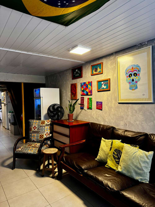 Área comum colorida no Hostel New Ipanema com sofás de couro preto, bandeira brasileira, arte folclórica e poltrona estampada