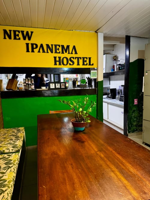 Recepção do Novo Hostel Ipanema com identidade visual em amarelo e verde, piso de madeira e decoração com plantas no Rio de Janeiro