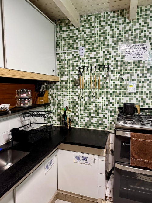 Cozinha da equipe da Pousada New Ipanema com azulejos verdes, bancadas pretas, fogão a gás e utensílios de cozinha no Rio de Janeiro