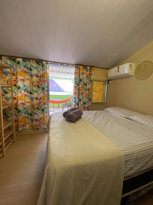 Quarto privativo na Pousada New Ipanema no Rio com camas de solteiro, cortinas coloridas e acesso à varanda com vista para o jardim