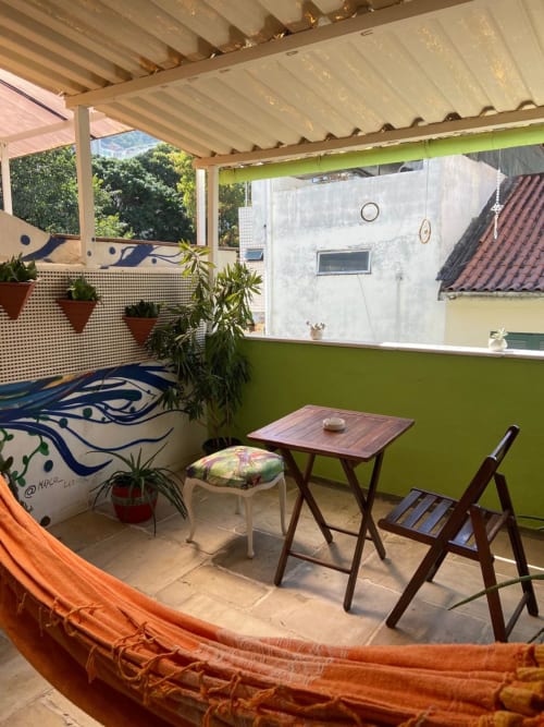 Varanda aconchegante em quarto privado do Hostel New Ipanema com rede, móveis de madeira, plantas exuberantes e vista para o jardim