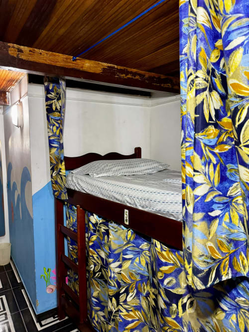 Cama em dormitório compartilhado com cortinas florais azuis e amarelas na Pousada New Ipanema, Rio de Janeiro