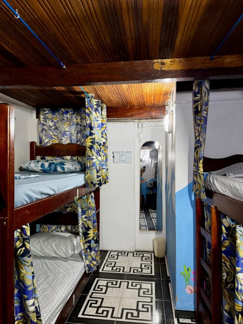 Dormitório compartilhado da Pousada New Ipanema no Rio de Janeiro com beliches, cortinas azuis e amarelas, teto de madeira