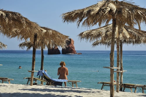 Spiaggia del Resort Baia Cea con ombrelloni in paglia, sabbia bianca, mare turchese e spettacolari formazioni rocciose