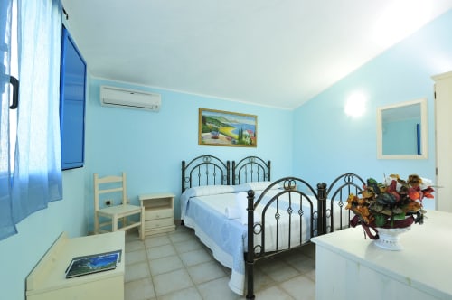 Camera da letto luminosa e azzurra al Resort Baia Cea con letto in ferro battuto, finestra, aria condizionata e bagno privato a Bari Sardo.