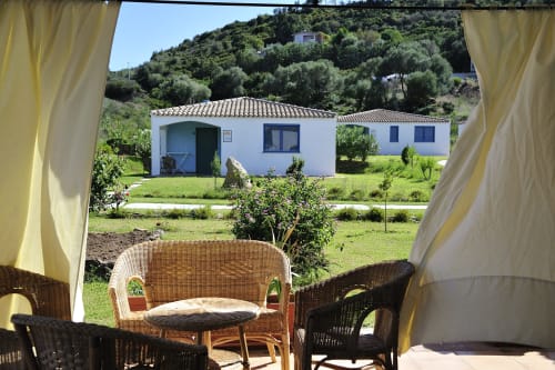 Patio di Resort Baia Cea con sedie in vimini affacciato su bungalow bianco e giardini mediterranei a Bari Sardo