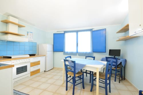 Luminosa zona cucina-pranzo al Resort Baia Cea di Bari Sardo con accenti blu, ripiani in legno e tavolo da pranzo