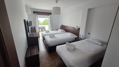 Quarto triplo do Hotel Slow Stay em Esposende com três camas, TV e varanda com vista para o rio