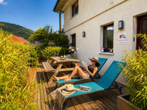 Un invité se détend sur des transats turquoise sur la terrasse en bois du Domaine des Fleurs à Gérardmer, avec vue sur les montagnes