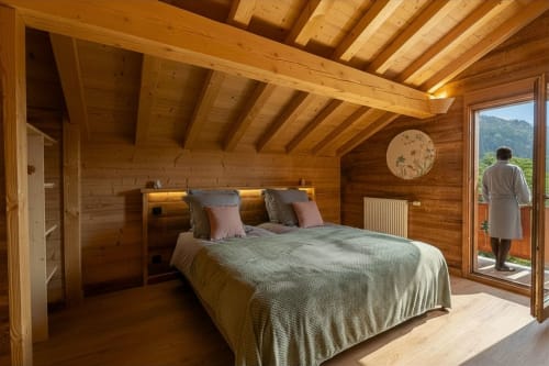 Chambre de chalet en bois au Domaine des Fleurs à Gérardmer avec lit queen, poutres apparentes et vue montagne par portes vitrées