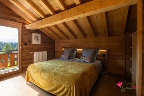 Chambre lumineuse du chalet Le Cœur de Marie au Domaine des Fleurs, Gérardmer, avec poutres en bois, literie jaune