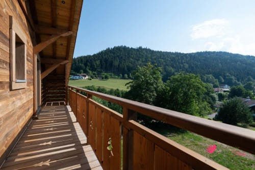 Balcon en bois du chalet Le Domaine des Fleurs surplombant la vallée de Gérardmer avec montagnes boisées et fleurs roses